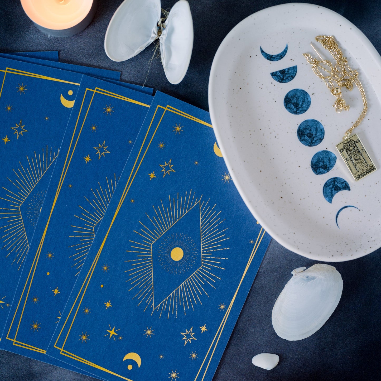 Tarot cards with sea shells, crustals and a ceramic plate with a moon cycle pattern.