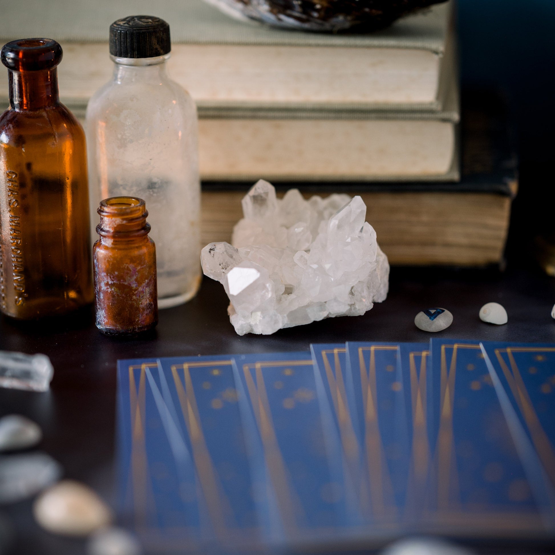 Tarot cards, crystals,  runes and glass bottles in front of a stack of books.